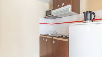 A kitchen with wooden cabinets, a microwave, a kettle, and a refrigerator.