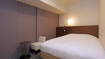 A hotel room with a large bed, a small round table, a chair, and a bedside lamp.