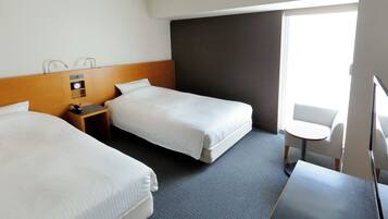 Une chambre d’hôtel avec deux lits, un bureau, une chaise, une petite table et une fenêtre.