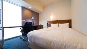A hotel room with a large bed, a desk with a chair, a lamp, and a view of the outdoors. - JR Inn Sapporo (Sapporo)