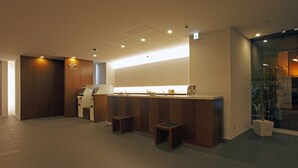 A reception area with a wooden reception desk, a small seating area, and a potted plant. - JR Inn Sapporo (Sapporo)