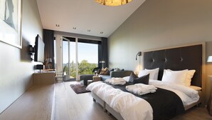 Een moderne hotelkamer met een groot bed, een sofa, een tafeltje en uitzicht op het groen.