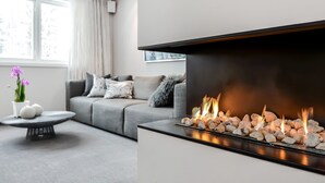 Een moderne woonkamer met een open haard, een grijze bank en een ronde salontafel met decoratieve objecten.