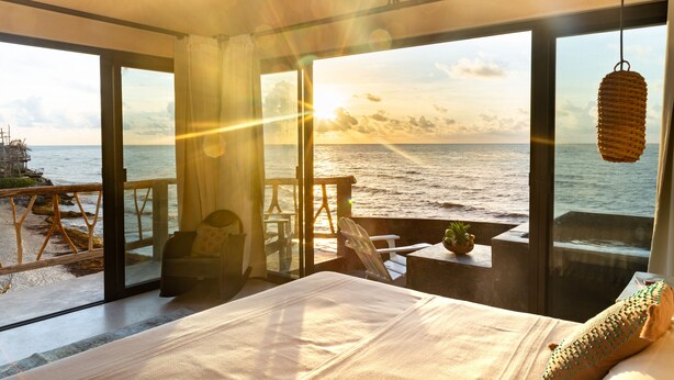 A bedroom with a large window overlooking the sea, a bed, and a small table with a plant. - La Posada del Sol Boutique Hotel Tulum (Tulum)