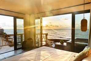 A bedroom with a large window overlooking the sea, a bed, and a small table with a plant. - La Posada del Sol Boutique Hotel Tulum (Tulum)