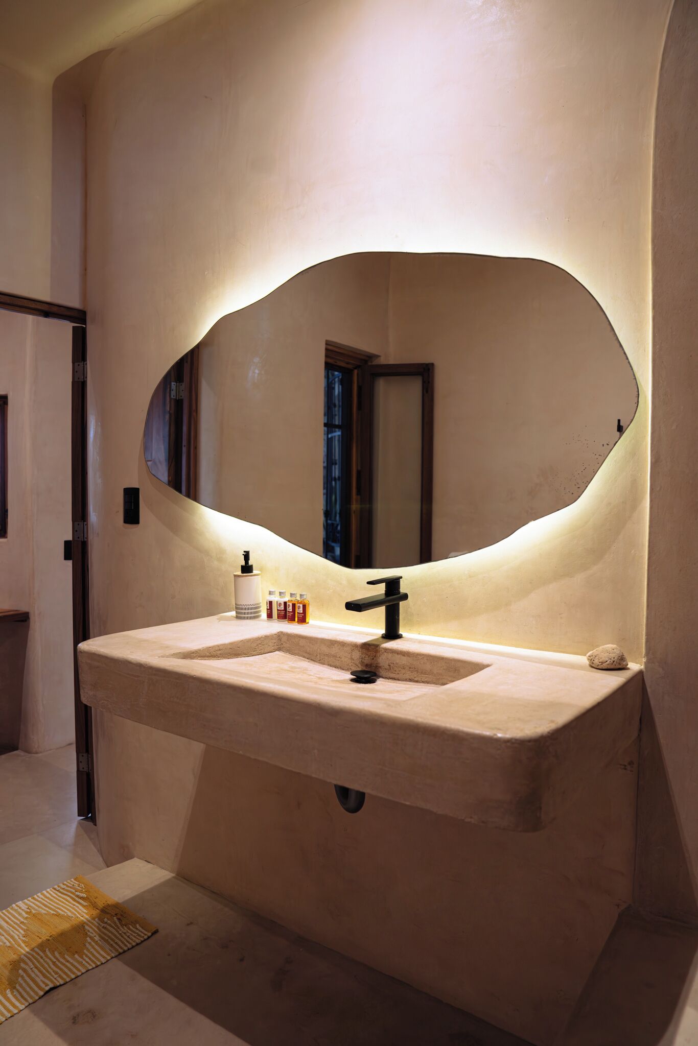 A bathroom with a large oval mirror, a beige sink, and a small bottle of hand soap on the counter.