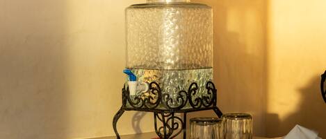 A water dispenser on a metal stand with a glass container, a bottle, and a tissue box.