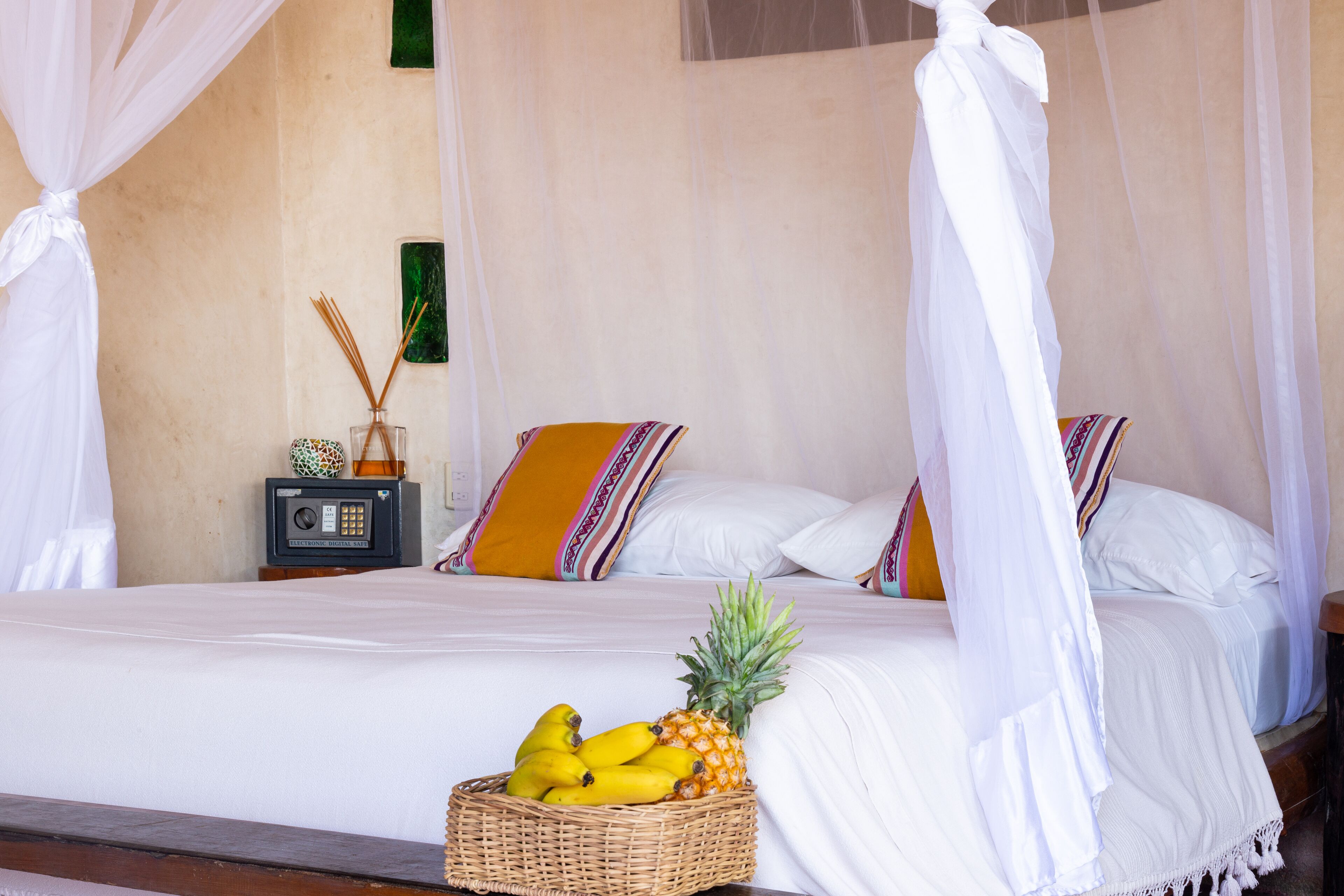 A bed with a canopy, a wicker basket with fruits, a radio, and decorative pillows.