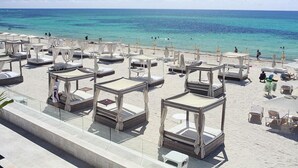 Um hotel à beira-mar com vários espreguiçadeiras e guarda-sóis, vista clara para o oceano e uma área de praia arenosa.