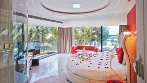 Een moderne hotelkamer met een groot bed, een balkon met uitzicht op palmbomen en een glazen scheiding tussen de kamer en het balkon.