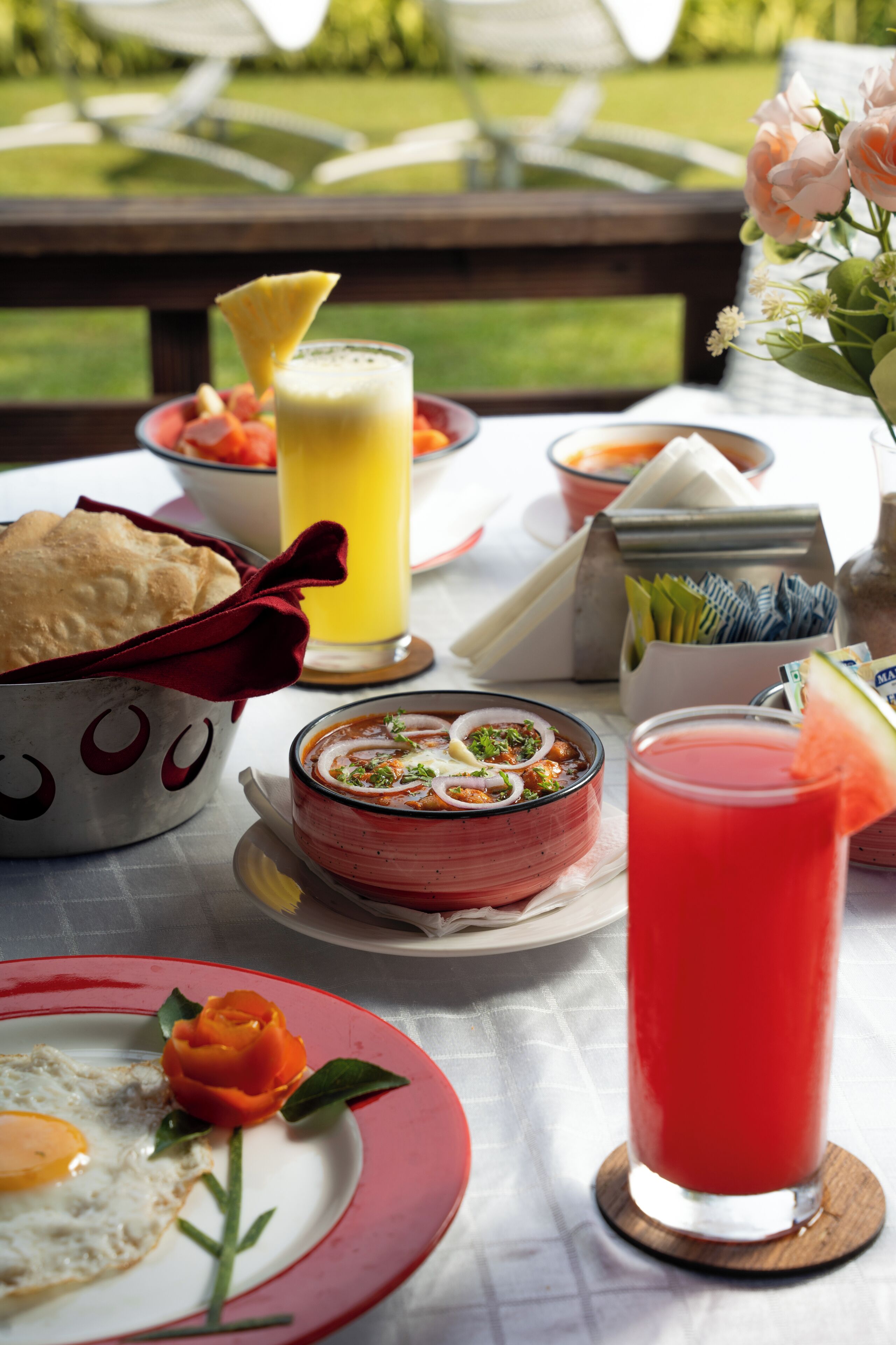 A table with food and drinks, including a bowl of soup, a plate with a fried egg and a rose, and a glass of red drink.