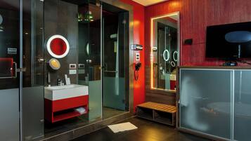 Ein modernes Badezimmer mit Duschkabine aus Glas, einem Waschtisch in Rot und Weiß, einer Sitzbank und einem großen Spiegel mit LED-Beleuchtung.
