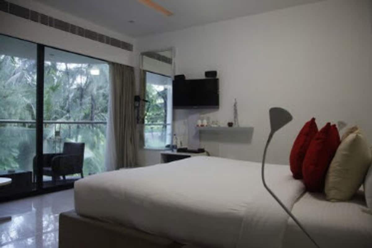A bedroom with a large bed, a flat-screen TV, and a view of greenery through the window.