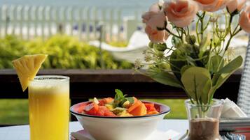 Una mesa con alimentos para el desayuno, como huevos, un frutero, un vaso de jugo de naranja y un jarrón con flores.