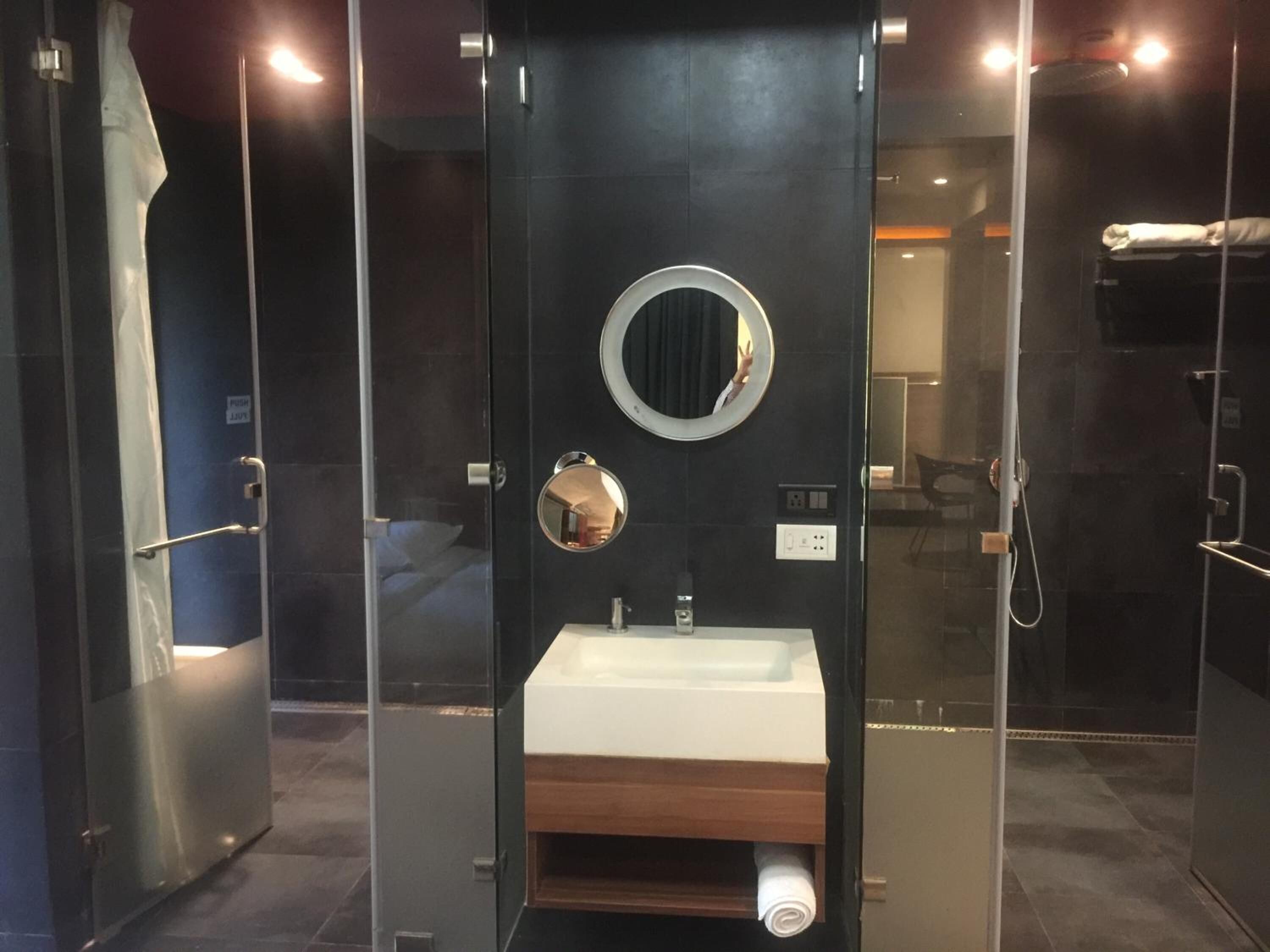 A modern bathroom with a glass enclosure, a round mirror, a white sink, and a towel rack.