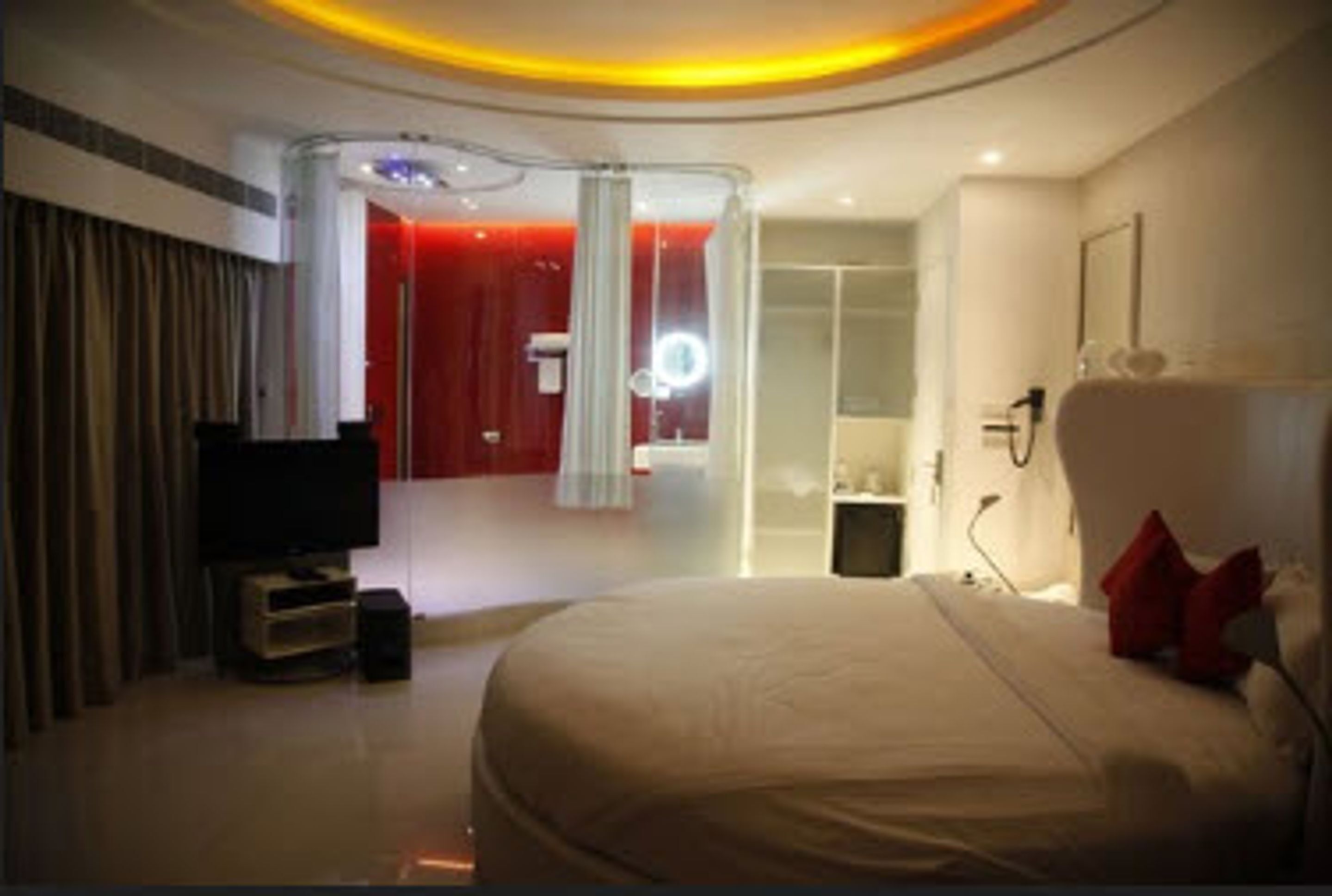 Une chambre d’hôtel moderne dotée d’un grand lit, d’une télévision, d’une coiffeuse avec un miroir et d’un mur d’accent rouge.