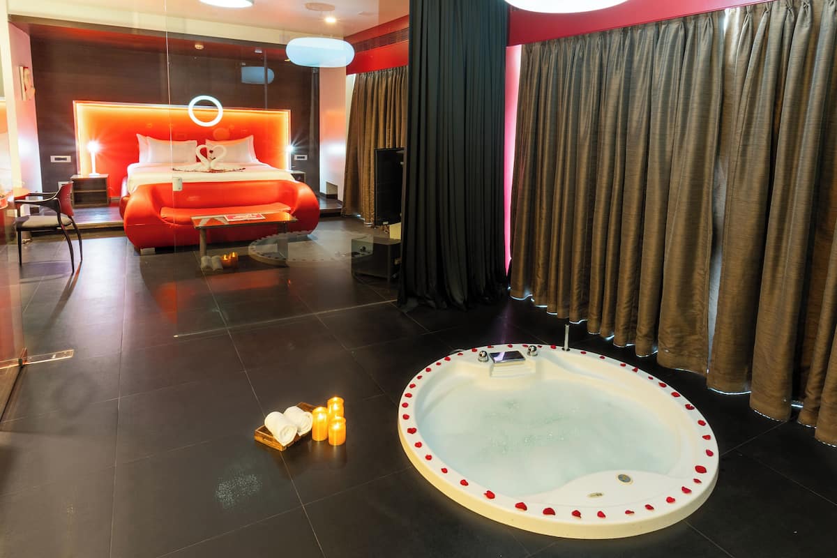 A modern hotel room with a large bed, a jacuzzi, and a seating area with a red sofa.