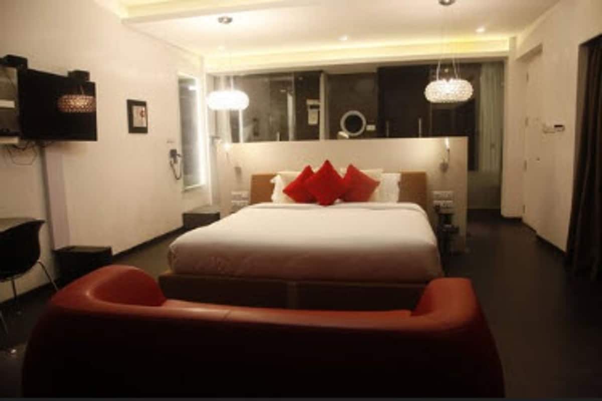 A modern hotel room with a large bed, a red accent chair, a TV, and a mirror.