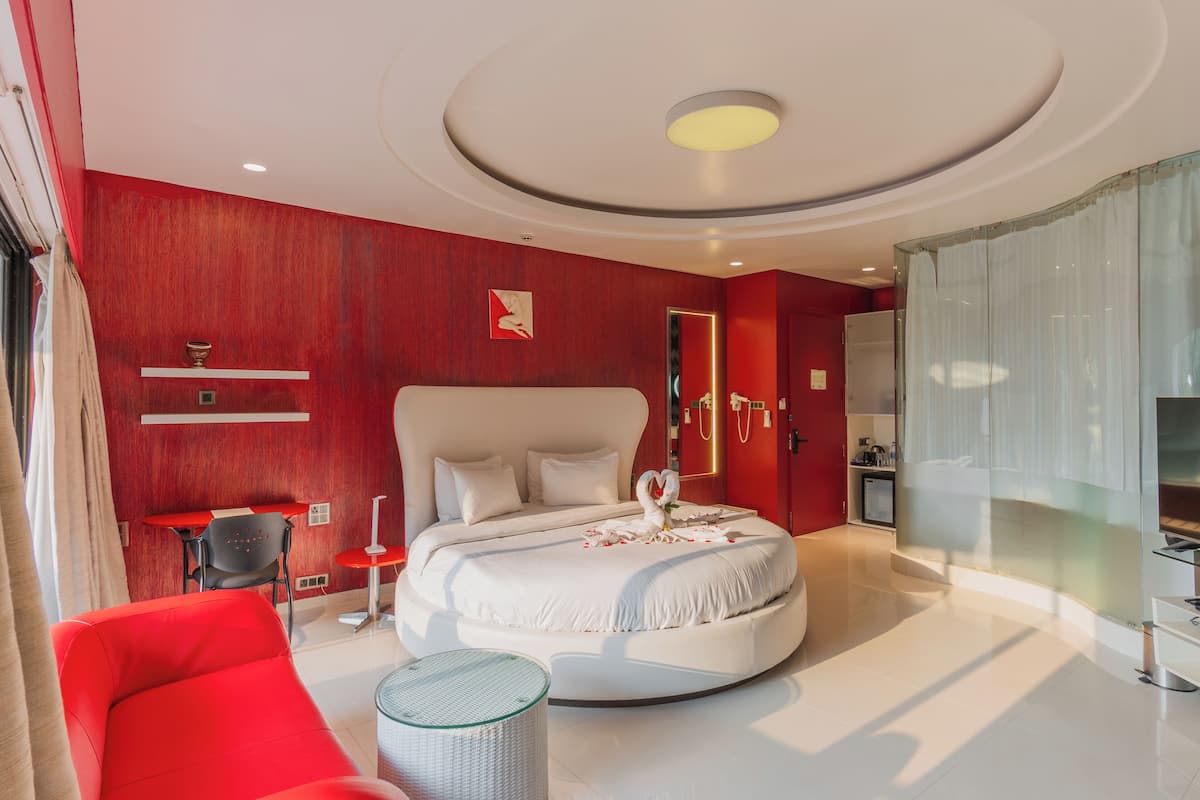 A modern bedroom with a round bed, red walls, and a glass shower enclosure.