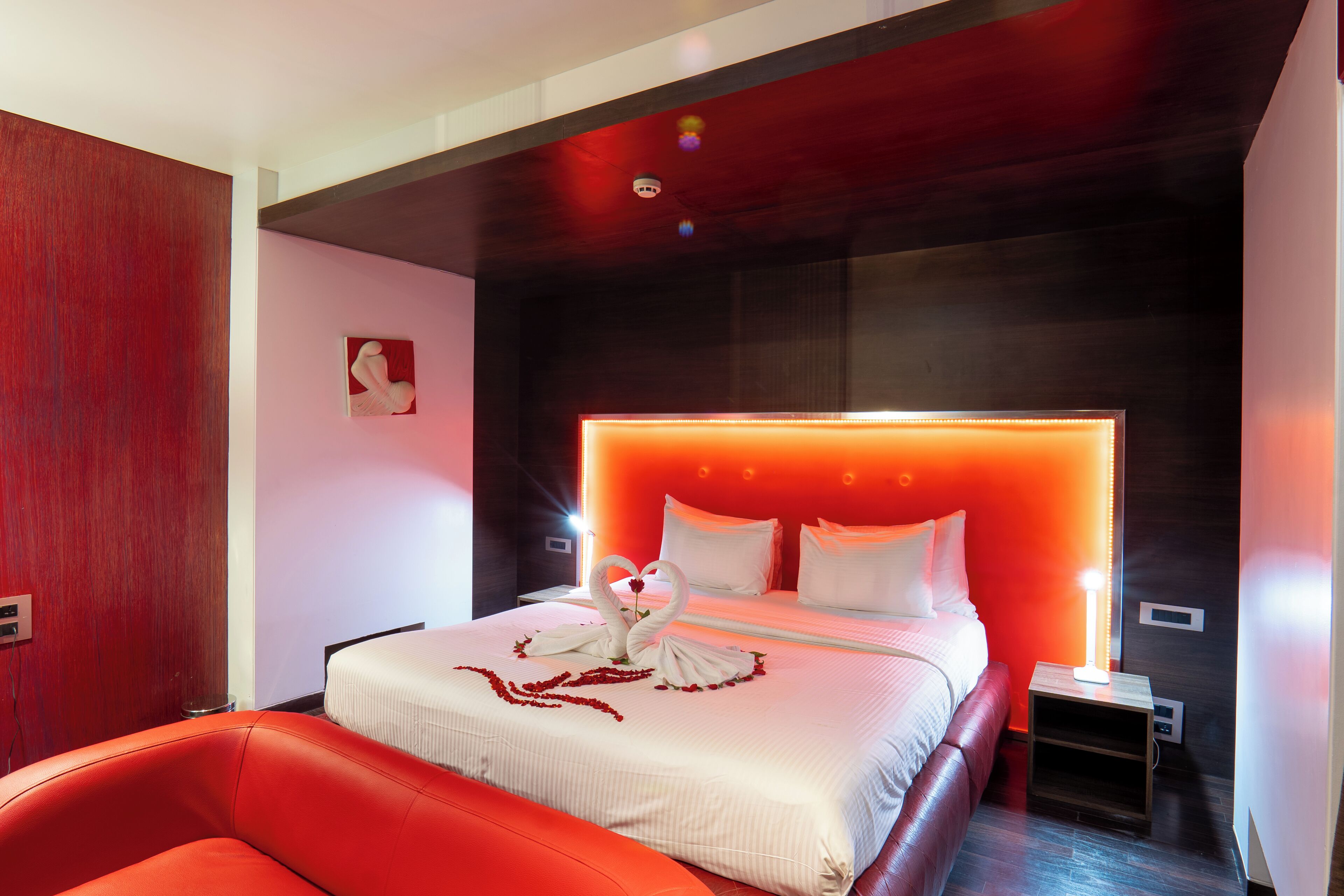Quarto de hotel moderno com uma cama grande, uma poltrona de couro vermelho e uma obra de arte na parede.