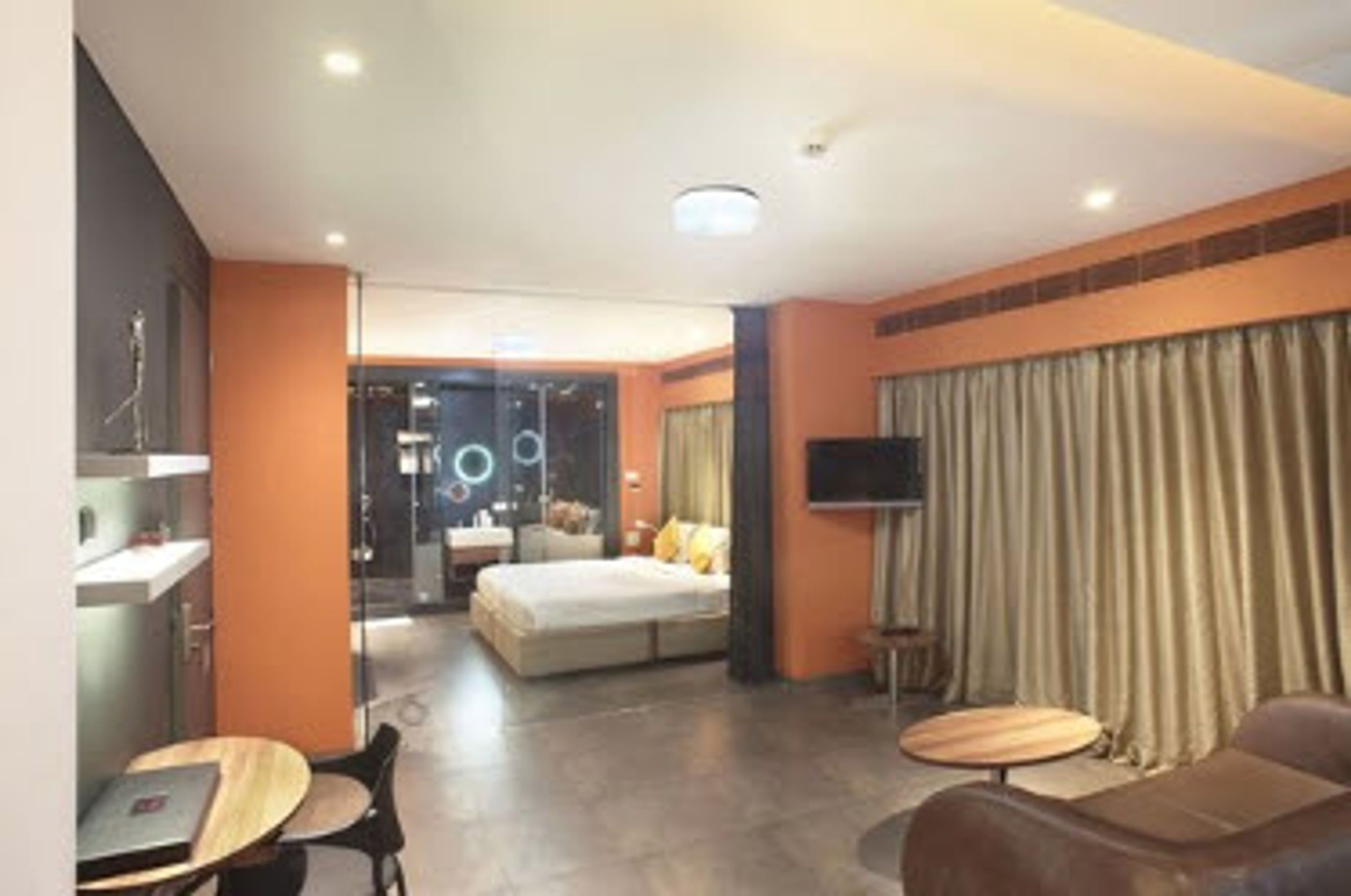 A modern hotel room with a bed, a seating area with a table and chairs, a TV, and a large window with curtains.