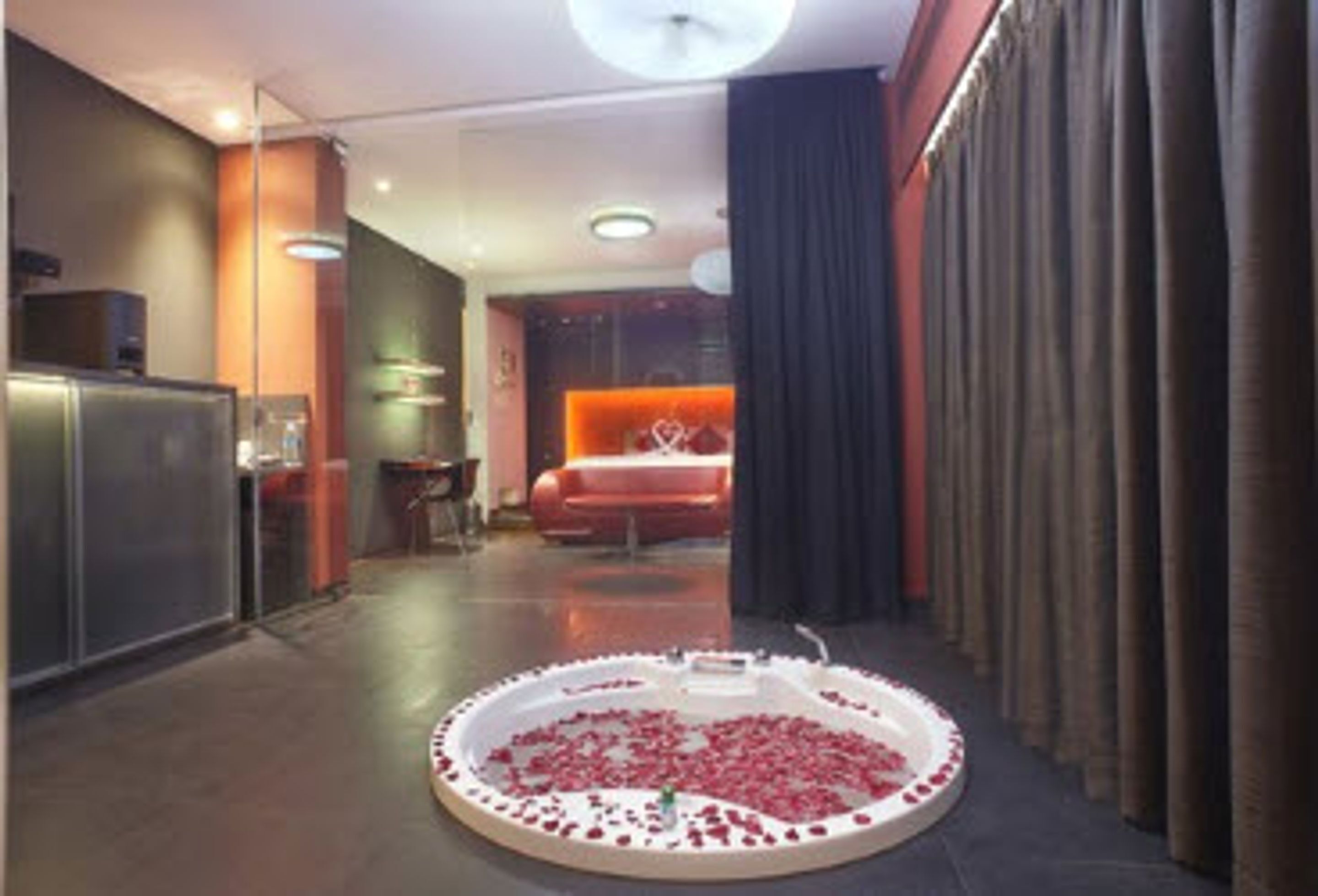 A hotel lobby with a circular seating area filled with rose petals, a reception desk, and a bed in the background.