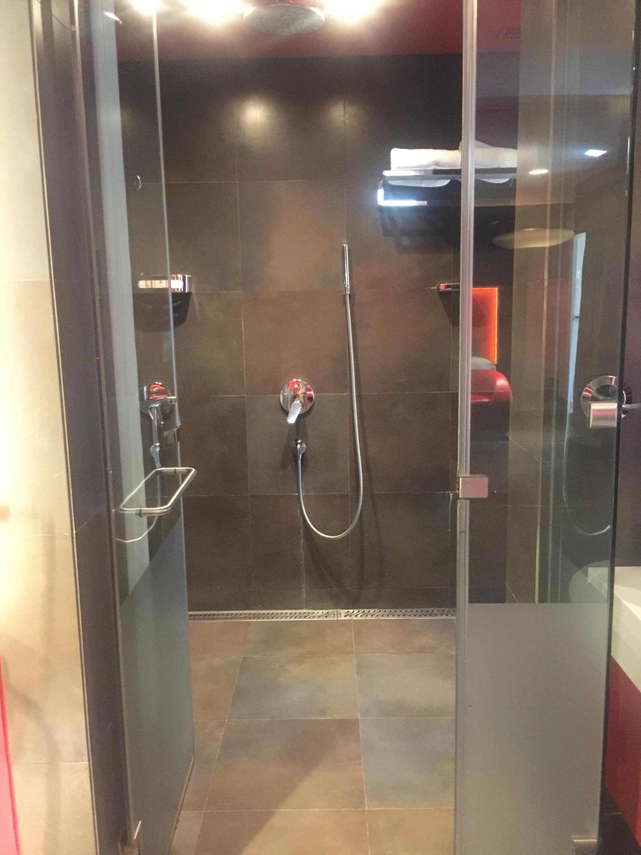 A glass-enclosed shower with a handheld showerhead and a wall-mounted faucet.