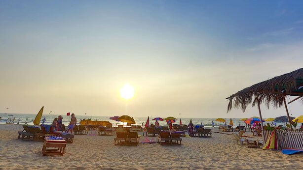 Een strand met ligbedden en parasols, een rieten constructie en de oceaan op de achtergrond.