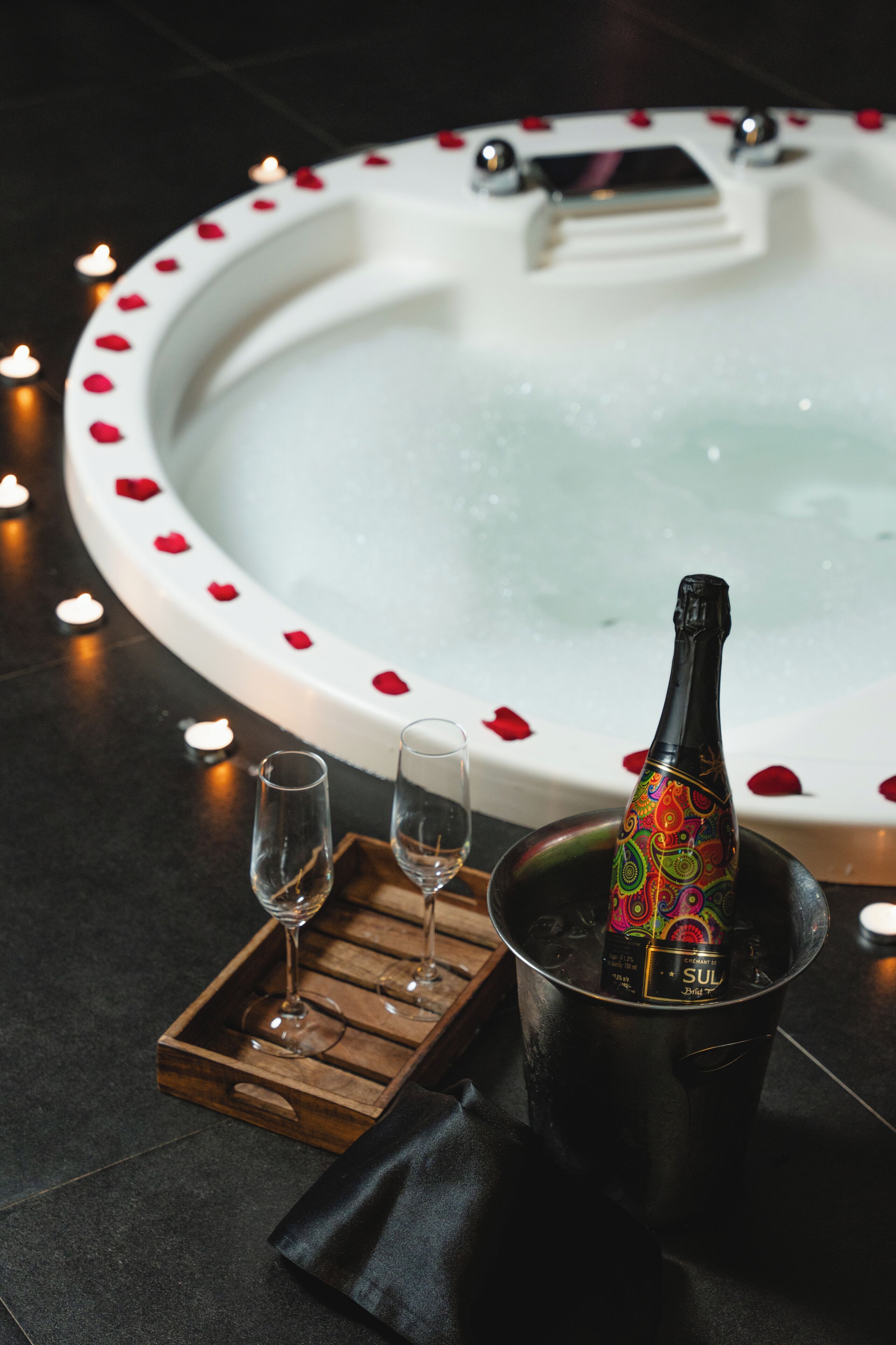 Un bain à remous parsemé de pétales de rose, une bouteille de champagne et deux verres sur un plateau.