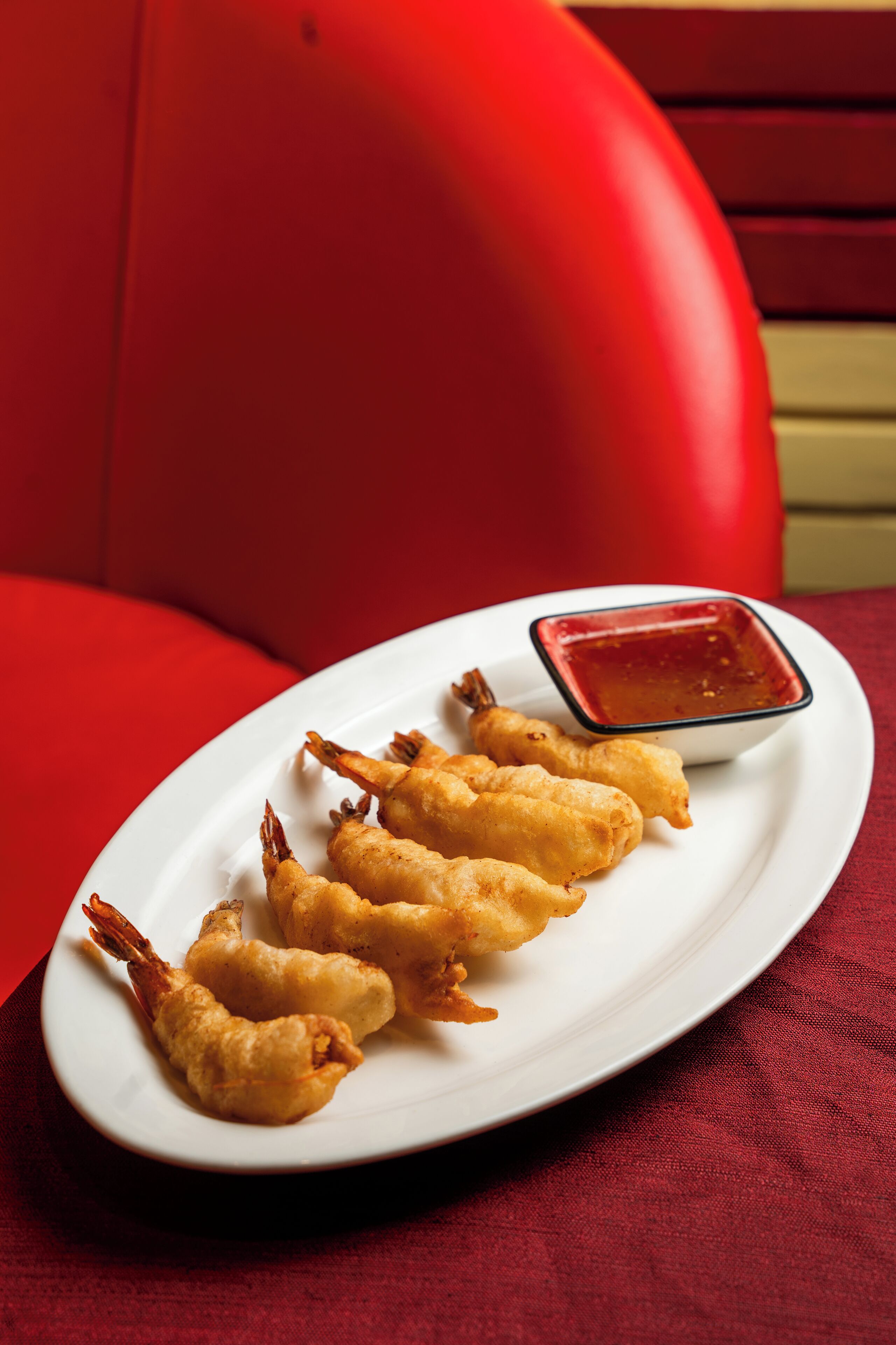 A white plate with fried shrimp and dipping sauce on a red tablecloth.