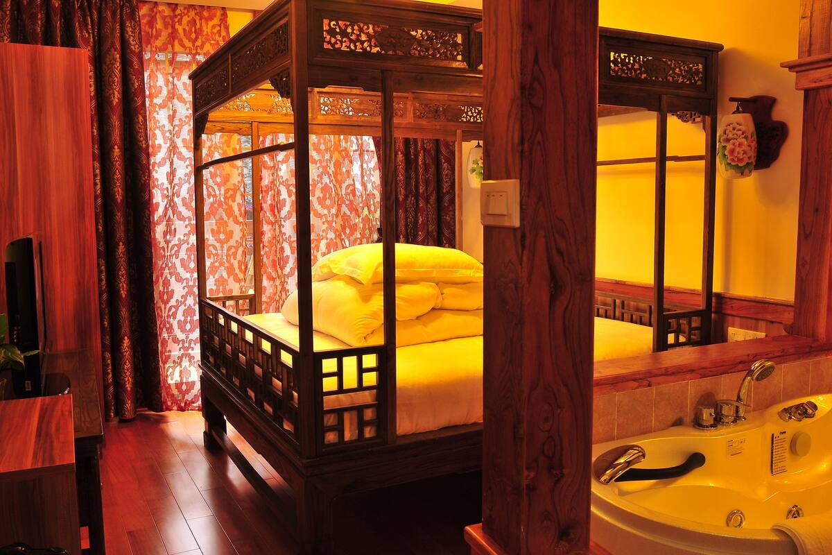 A traditional four-poster bed with a canopy, a wooden bench, a large mirror, and a bathtub.