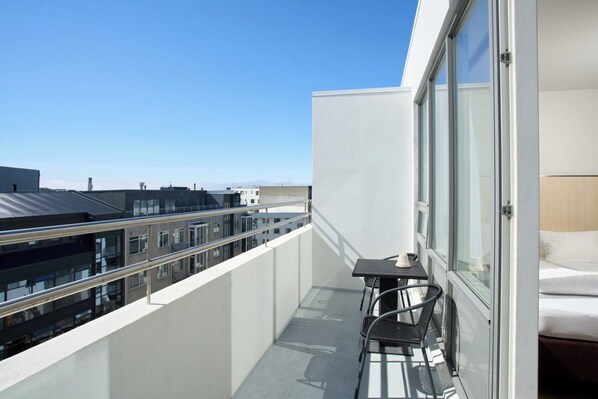 Un balcón con mesa y sillas, una cama y vistas a otros edificios.