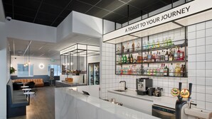 A modern bar area with a white counter, shelves of various beverages, and a sign that reads "A TOAST TO YOUR JOURNEY". - Hotel Klettur (Reykjavik)