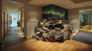 A hotel lobby with a large rock feature, wooden flooring, and a wall mural of the Northern Lights. - Hotel Klettur (Reykjavik)