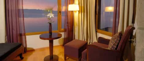 Una habitación con cama, una mesa redonda con un florero, una silla y vista a un cuerpo de agua a través de una ventana.