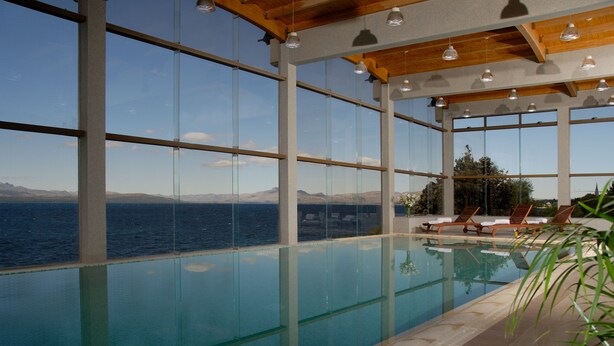 Une piscine intérieure dotée de grandes fenêtres offrant une vue sur la mer et les montagnes.