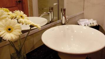 A bathroom with a white sink, a mirror, and a vase with white flowers.