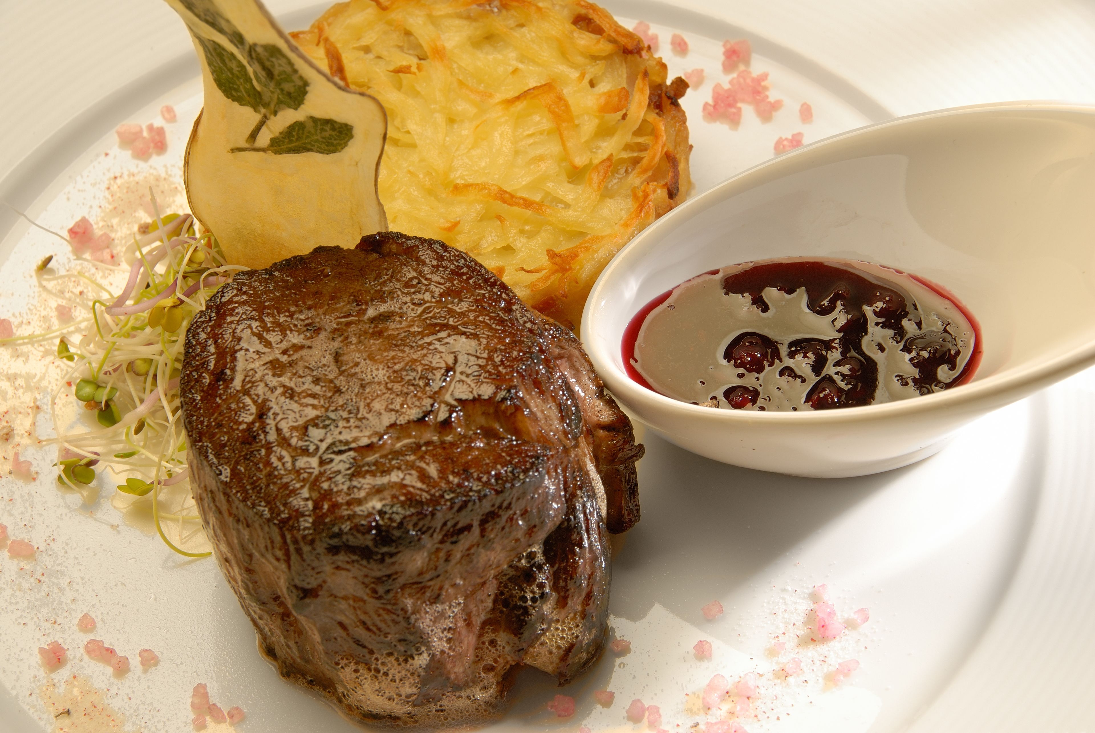 Une assiette avec un steak, un plat de pommes de terre et un bol de sauce.