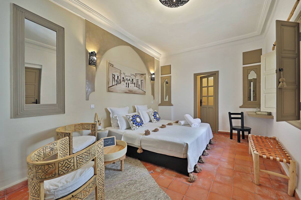 A bedroom with a bed, a chair, a small table, and a mirror.