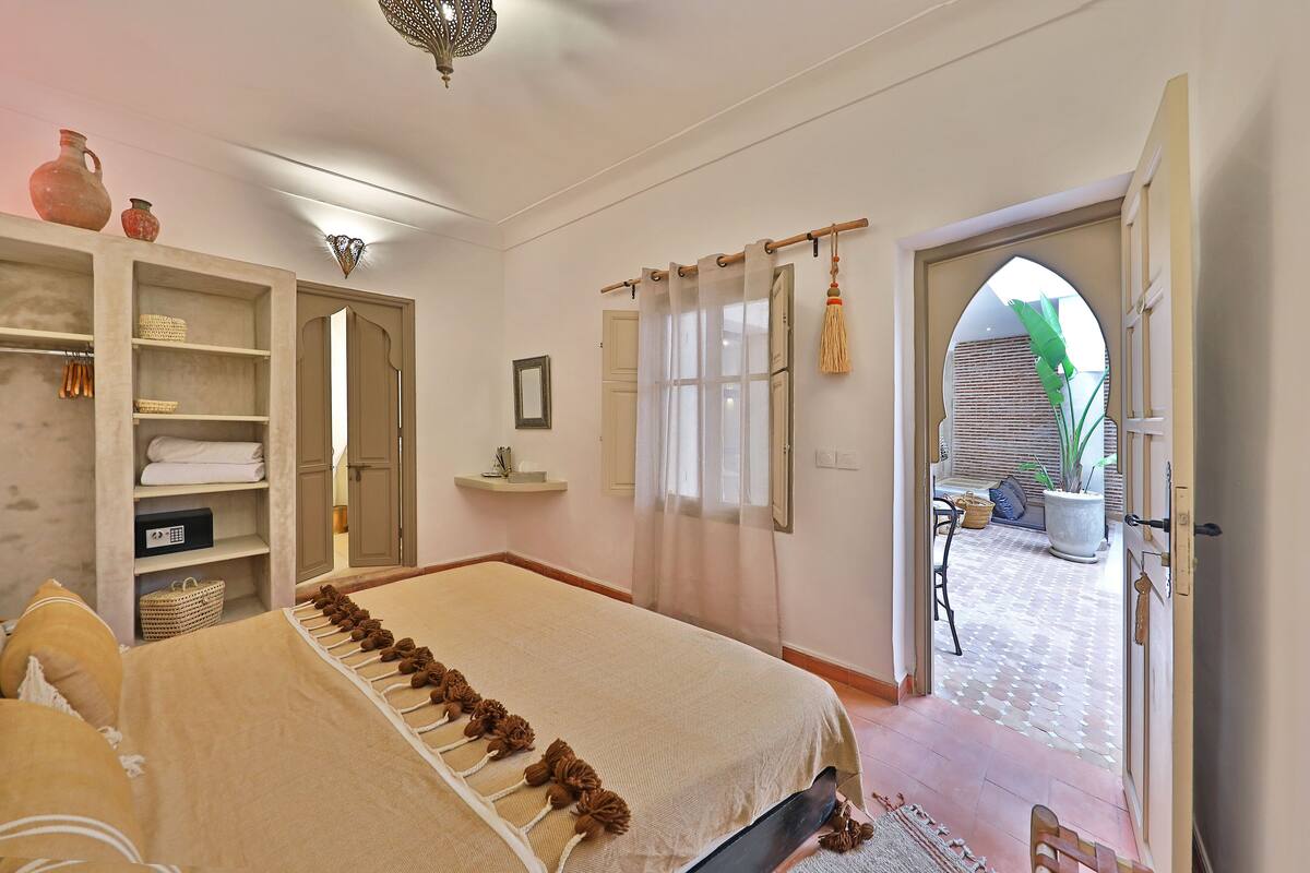 A bedroom with a bed, a wardrobe, a mirror, and a view of the outside.