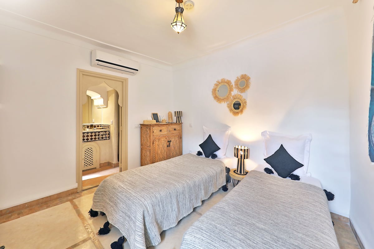 A room with two beds, a wardrobe, a mirror, and a wall-mounted air conditioner.