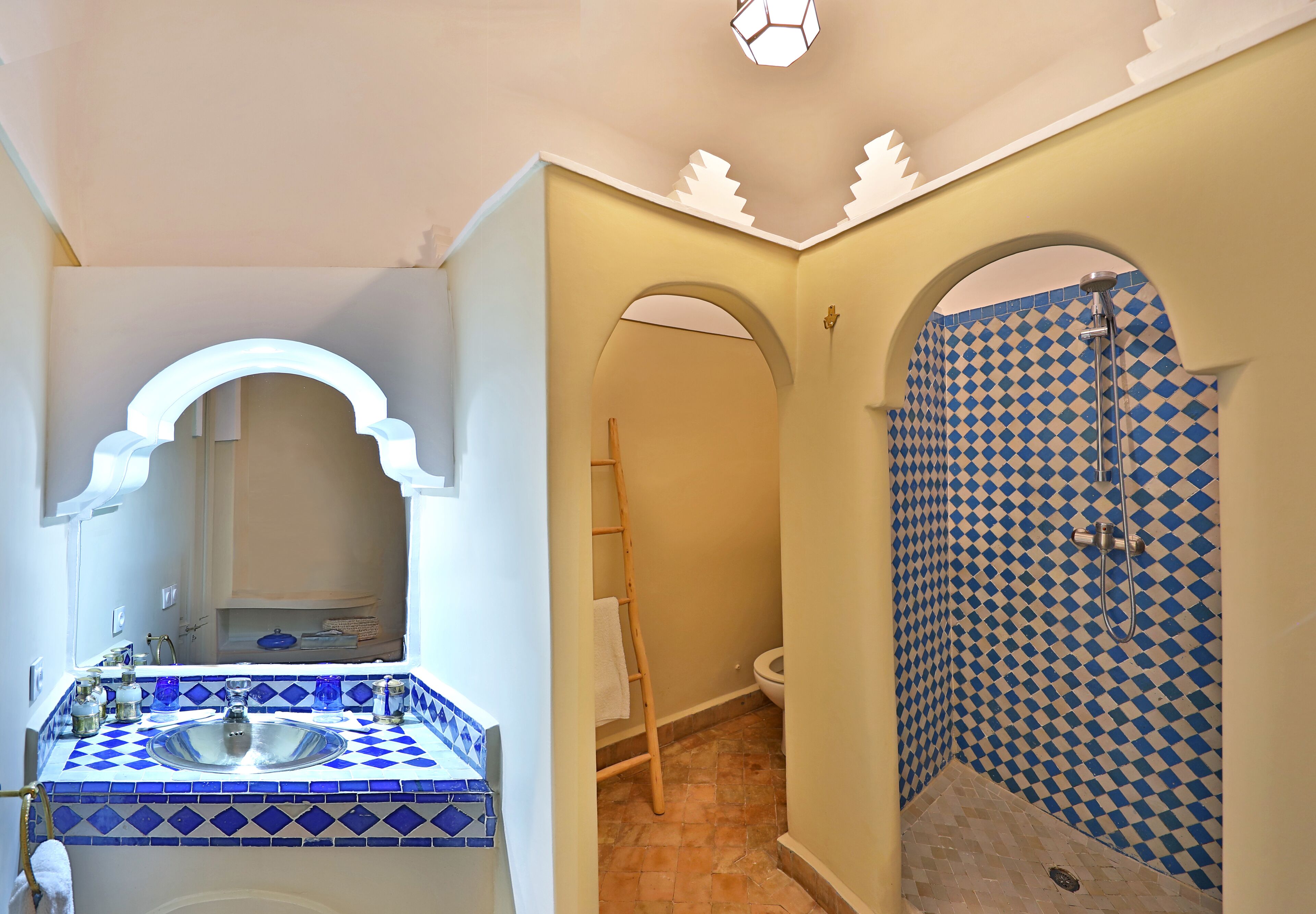 Un baño con un salpicadero de azulejos blancos y azules a cuadros, un lavamanos blanco y una ducha con pared de azulejos blancos y azules a cuadros.