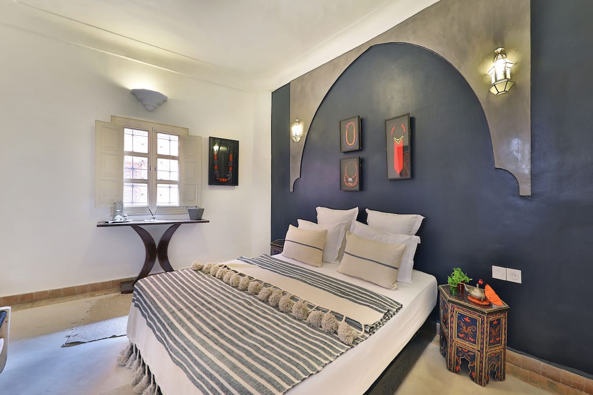 A bedroom with a bed, a nightstand, a desk, and a window.