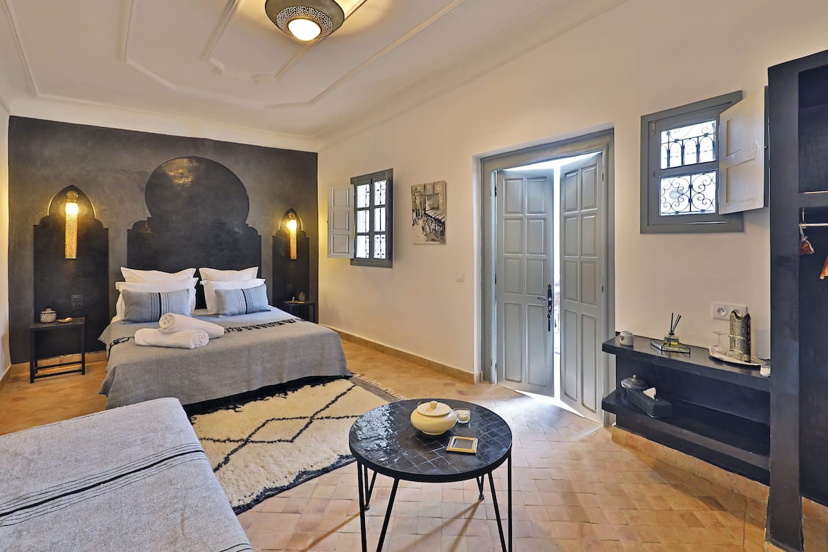 A bedroom with a bed, bedside tables, a small round table, a rug, and a door leading to another room.