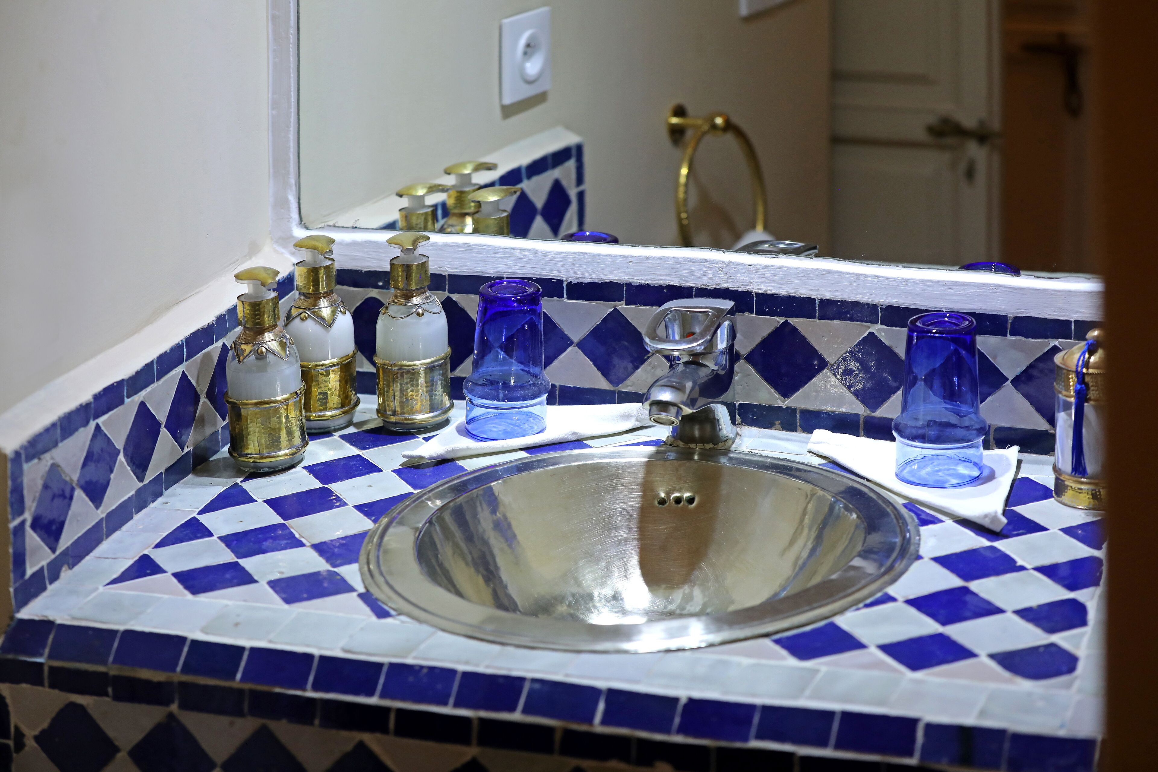 A bathroom with a blue and white checkered tile backsplash, a stainless steel sink, and various toiletries on the counter.