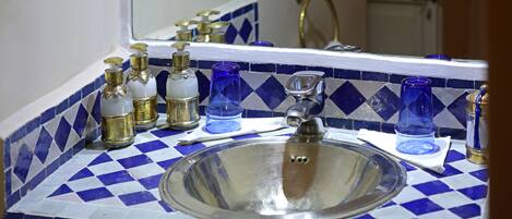 A bathroom with a blue and white checkered tile backsplash, a stainless steel sink, and various toiletries on the counter.