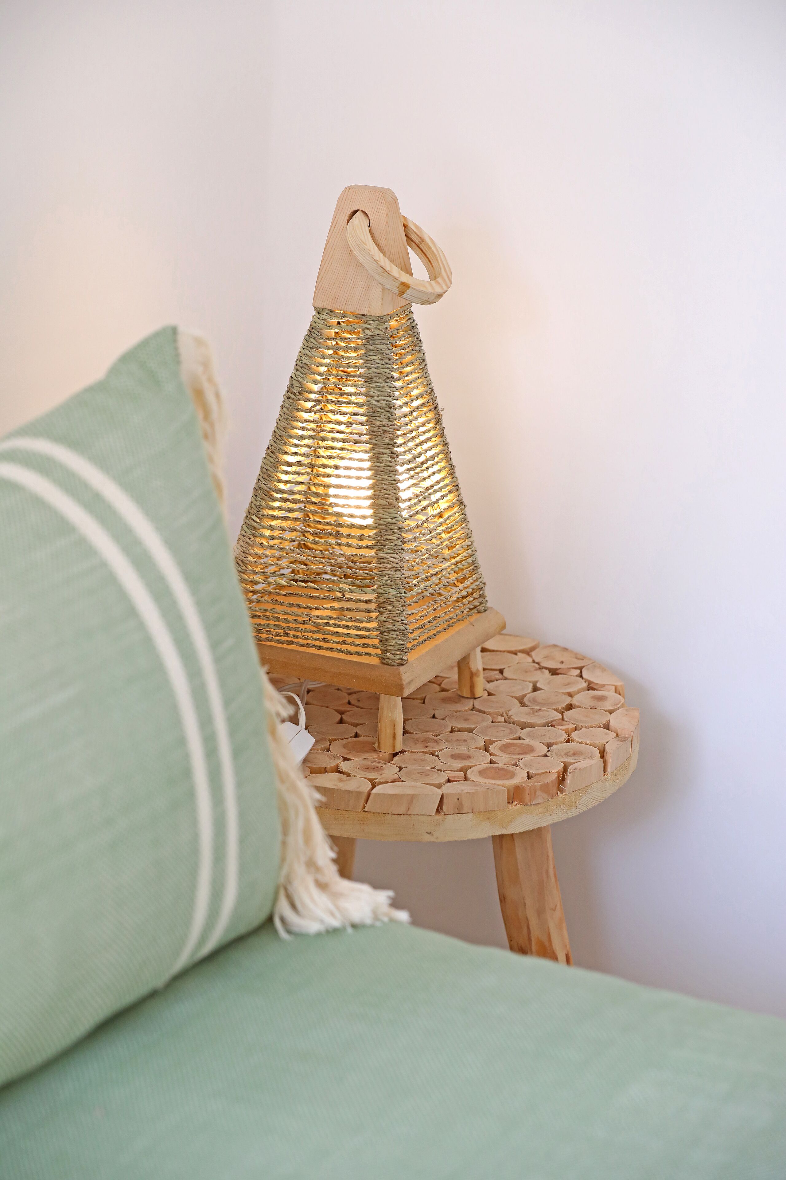 A wooden table with a woven lamp and a green cushion.