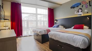 A hotel room with two beds, a desk, a chair, and a large window with red curtains.