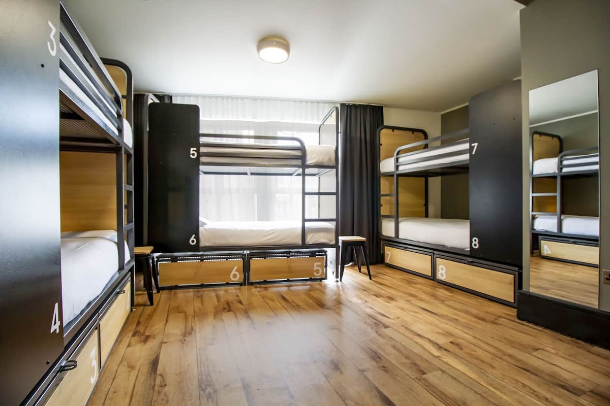 A train compartment with bunk beds, wooden flooring, and a window with curtains.