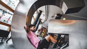 Iemand gebruikt een cirkelvormig trainingsapparaat in een sportschool, met zichtbare leidingen en apparatuur.